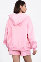 Woman wearing oversized soft pink hoodie with dropped shoulders and ribbed cuffs paired with matching shorts