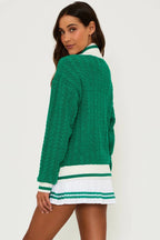 Woman wearing green cable knit sweater with white and green striped cuffs and collar paired with white pleated skirt
