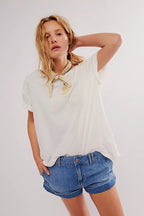 Woman wearing a boxy white tee with rolled sleeves and denim shorts, styled with a light neck scarf in casual fashion.