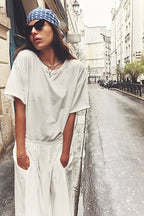 Woman wearing a loose white tee paired with white pants and a blue polka dot headscarf in an urban street setting