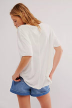 Woman wearing a loose white tee and denim shorts, shown from the back in casual women's clothing style.