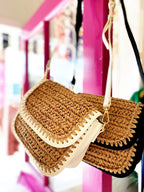 Crossbody woven bags with vegan leather trim, hanging on display in a bright boutique setting.