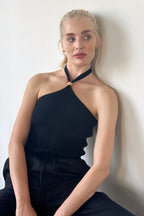 Woman wearing black ribbed halter top with wooden bead detail and high neck tie, styled with black pants.