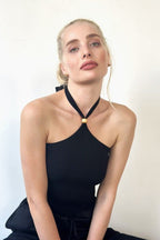 Woman wearing a black ribbed halter top with a wooden bead detail at the tie-up high neck in women's clothing.
