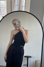 Woman wearing a black ribbed halter top with tie-up neck, taking a mirror selfie in minimal indoor setting.