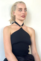 Woman wearing a black ribbed halter top with wooden bead detail and tie-up neck, styled for women's clothing.