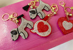 Rhinestone-studded dog and heart shaped keychains with gold rings and small tassel accents on pink surface