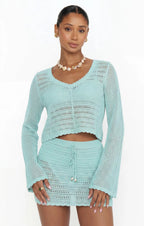 Woman wearing light blue crochet knit top with long sleeves and matching mini skirt in women's clothing style