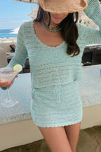 Woman wearing light blue crocheted top and skirt set holding cocktail at beachside bar in women's clothing style