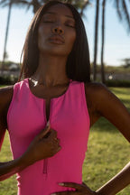 Woman wearing a bright pink sleeveless romper with front zipper outdoors in a sunny park setting