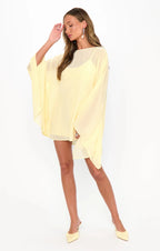 Woman wearing a flowing pale yellow mini dress with wide sleeves and matching pointed-toe heels in women's clothing style