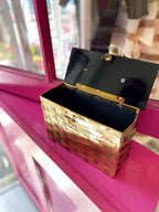 Brass woven vintage handbag with black interior, open on a bright magenta window ledge, stylish accessory for women.