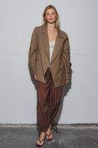 Woman wearing an oversized brown blazer paired with loose brown pants and sandals against plain background