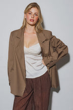 Woman wearing a brown oversized blazer over a white camisole and textured brown pants in a studio setting
