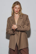 Woman wearing a brown oversized blazer styled with wide-legged pants in a minimal studio setting