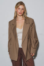 Woman wearing a loose brown oversized blazer over a white top and brown pants in a studio setting