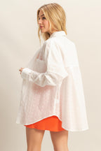 Woman wearing a loose white eyelet shirt with long sleeves over an orange skirt in a side view