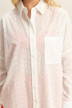 Close-up of a white oversized eyelet button-down shirt with collar, front pocket, and floral cutout details.