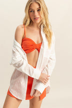 Woman wearing a white eyelet oversized shirt over a bright orange crop top and matching skirt in women's clothing style.