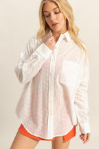 Woman wearing oversized white eyelet button-down shirt with collar and chest pocket paired with orange shorts