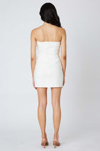 Woman wearing a white strapless mini dress with a back zipper, standing facing away on a plain background