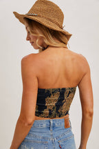 Woman wearing a brown patterned satin tube top paired with blue denim jeans and a woven straw hat from the back view