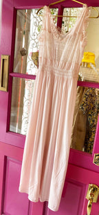 Light pink maxi dress with delicate lace detailing and ruffled shoulders hanging on a door in a clothing store.