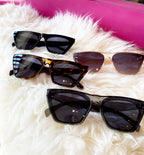 Four pairs of stylish women's sunglasses with UV 400 protection displayed on white fur against a pink background
