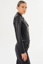 Woman wearing a fitted black leather moto jacket with a diagonal zip and snap collar in a side profile pose