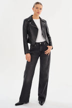 Woman wearing a fitted black leather moto jacket with a white shirt and black high-waisted jeans in a studio setting