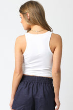 Woman wearing a white sleeveless tank top and navy blue shorts, seen from the back in casual women's clothing.