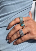 Close-up of hand wearing gold rings with blue and green gemstones on striped blue fabric background