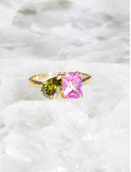 14K gold ring with bright pink and green gemstones on a white textured surface