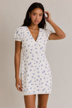 Woman wearing a white mini dress with blue floral print and puff sleeves in women's clothing fashion.