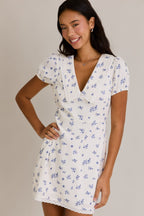 Woman wearing a white mini dress with small blue floral print and puff sleeves in women's clothing fashion.