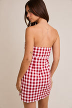 Woman wearing red and white checkered strapless mini dress in a plain background, showcasing back view.