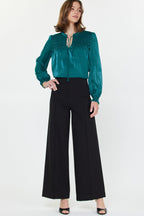 Woman wearing high-waisted black wide-leg pants paired with a teal long-sleeve blouse in women's clothing style