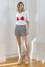 Young woman modeling a white tee with red bikini graphic paired with black and white striped shorts in natural light