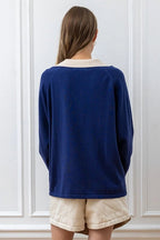 Woman wearing a navy blue knit pullover with a cream collar, paired with light beige shorts, shown from the back.