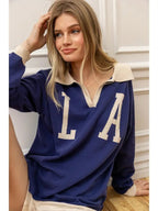 Woman wearing a navy blue knit pullover with beige collar and large letters, casual women's clothing style.