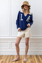 Woman wearing a navy knit pullover with white collar and cuffs paired with cream shorts and a tan bucket hat