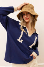 Woman wearing navy knit pullover with cream collar and cuffs, paired with a tan woven bucket hat.
