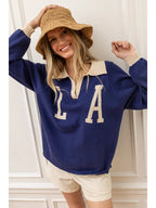 Woman wearing a blue knit pullover with cream collar and cuffs, paired with beige shorts and a woven bucket hat