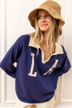 Woman wearing navy knit pullover with beige collar and large letters, paired with a woven sun hat in casual women's clothing style.