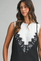 Woman wearing sleeveless top with black lace overlay detail on white fabric, styled for women's clothing fashion.