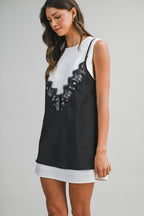 Woman wearing a black lace overlay mini dress layered over a white sleeveless underdress in women's clothing style