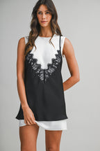 Woman wearing a black lace overlay tank top over a white mini dress in a studio setting.
