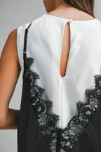 Close-up of a woman’s back wearing a black lace overlay tank top over a white garment with a button closure.