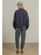 Woman wearing a dark bomber jacket paired with loose gray jeans and brown ankle boots, seen from the back