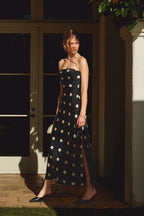 Woman wearing a strapless black maxi dress with white polkadots standing outdoors in sunlight